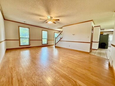 Unfurnished room with crown molding, light wood-type flooring, a ceiling fan, healthy amount of natural light, and stairs
