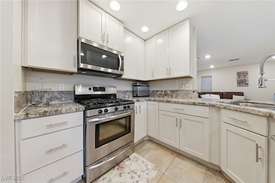 Kitchen with stainless steel appliances, white cabinetry, light stone countertops, light tile patterned floors, and recessed lighting