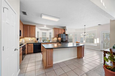Bright kitchen with wooden cabinets, central island, and tiled flooring.