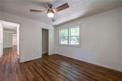 Unfurnished bedroom with a textured ceiling, dark wood-style floors, baseboards, a closet, and ceiling fan