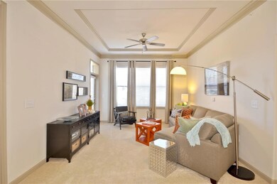 Carpeted living room with crown molding, ceiling fan, and a raised ceiling