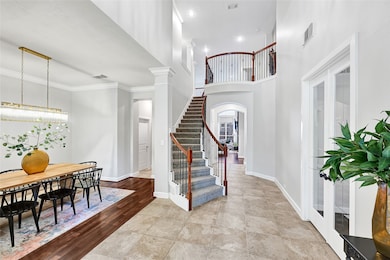 This inviting entryway features a grand staircase with elegant railings, a dining area with a modern light fixture, and spacious high ceilings. The mix of tile and wood flooring adds warmth and sophistication to the space.