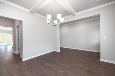 Empty room with a chandelier, beamed ceiling, dark wood finished floors, and baseboards