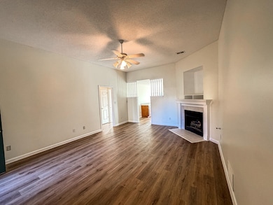 Unfurnished living room featuring ceiling fan, a textured ceiling, dark wood-style floors, a tile fireplace, and baseboards