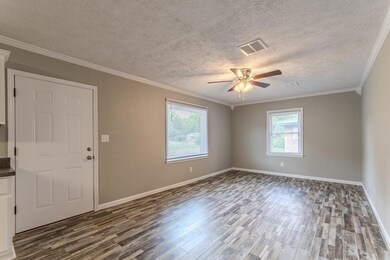 Unfurnished room featuring healthy amount of natural light, dark wood-style floors, ceiling fan, crown molding, and a textured ceiling