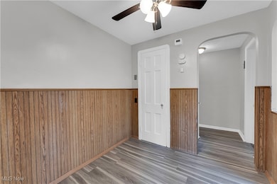 Unfurnished room featuring wainscoting, a ceiling fan, wooden walls, wood finished floors, and arched walkways