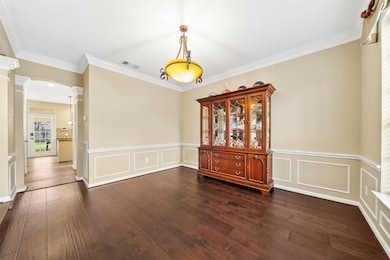The formal dining area also features espresso-stained hardwood flooring, wainscot trim, crown moulding, bronze lighting fixture, and pass-through access to the kitchen area.