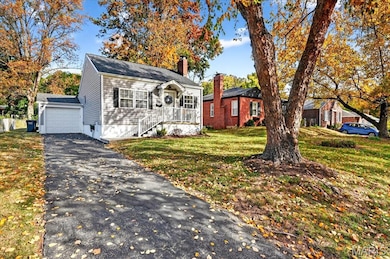 Bungalow-style house featuring a chimney, a front yard, a garage, driveway, and an outdoor structure
