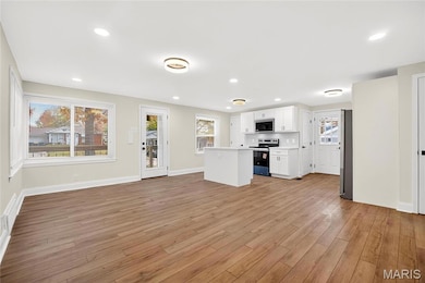Kitchen with white cabinets, light countertops, stainless steel appliances, open floor plan, and light wood-style flooring