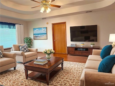 Living room featuring wood finished floors, a ceiling fan, and a tray ceiling