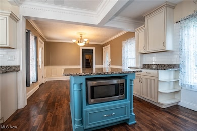 Kitchen with tasteful backsplash, blue cabinetry, stainless steel microwave, a center island, and crown molding