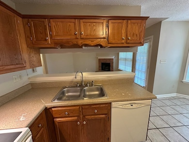 Kitchen featuring dishwasher, a sink, a peninsula, brown cabinets, and light tile patterned floors