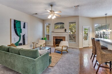 Living room featuring a chandelier, a tile fireplace, a textured ceiling, wood finished floors, and a ceiling fan