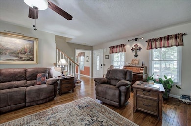 Living room with a textured ceiling, dark wood finished floors, a ceiling fan, and stairway