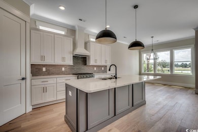 Kitchen with a sink, wall chimney exhaust hood, backsplash, ornamental molding, and white cabinetry