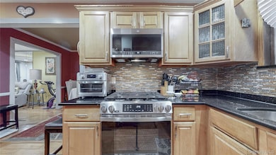 Kitchen with appliances with stainless steel finishes, crown molding, backsplash, dark stone countertops, and glass insert cabinets