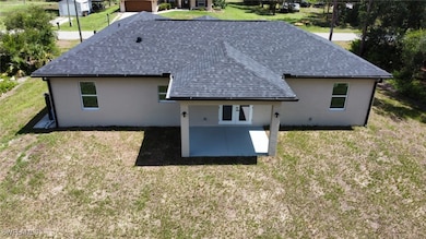 Back of property featuring a shingled roof, a patio area, stucco siding, and a lawn