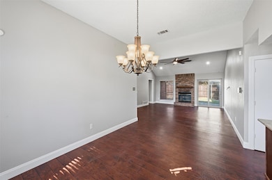 Unfurnished living room with vaulted ceiling, a brick fireplace, dark wood finished floors, a chandelier, and a ceiling fan