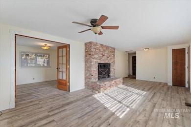 Unfurnished living room featuring light wood-style floors, a brick fireplace, and ceiling fan