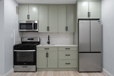 Kitchen with stainless steel appliances, backsplash, light stone counters, light wood-style flooring, and green cabinetry