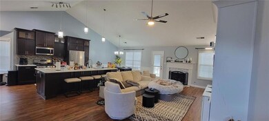 Living room featuring a ceiling fan, dark wood-style floors, a fireplace, high vaulted ceiling, and a chandelier