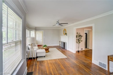 Living area with ornamental molding, wood finished floors, a fireplace with flush hearth, and ceiling fan