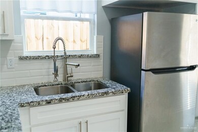 Kitchen with freestanding refrigerator, white cabinetry, backsplash, and light stone countertops