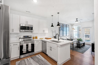 Kitchen featuring appliances with stainless steel finishes, a peninsula, hanging light fixtures, backsplash, and white cabinetry