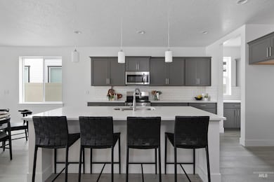 Kitchen with tasteful backsplash, hanging light fixtures, gray cabinetry, a kitchen island with sink, and light wood-style flooring