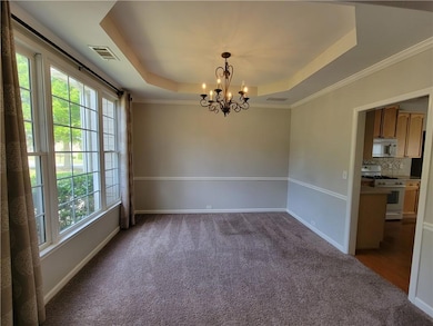 Unfurnished room with an inviting chandelier, a tray ceiling, baseboards, and visible vents