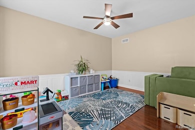 Game room featuring dark wood-type flooring, a wainscoted wall, a decorative wall, and a ceiling fan