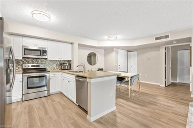 Kitchen featuring stainless steel appliances, a sink, a peninsula, a textured ceiling, and white cabinetry