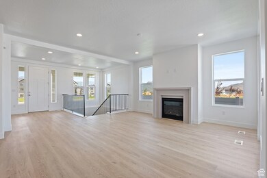 Unfurnished living room featuring light wood-type flooring, a glass covered fireplace, plenty of natural light, recessed lighting, and a textured ceiling