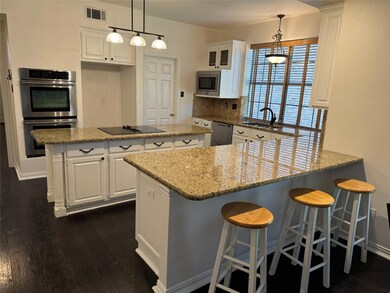 Gourmet Kitchen with hanging light fixtures, island, eat-in counter, stainless steel double ovens plus microwave, white cabinetry, and dark hardwood floors
