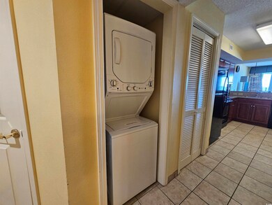 Laundry room with light tile patterned floors, a textured ceiling, and stacked washing machine and dryer