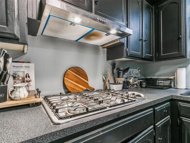Kitchen featuring under cabinet range hood, stainless steel gas stovetop, and dark cabinets