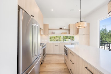 Kitchen featuring light brown cabinetry, modern cabinets, stainless steel appliances, light stone counters, and recessed lighting
