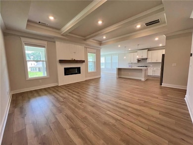 Unfurnished living room featuring crown molding, plenty of natural light, wood finished floors, a glass covered fireplace, and baseboards