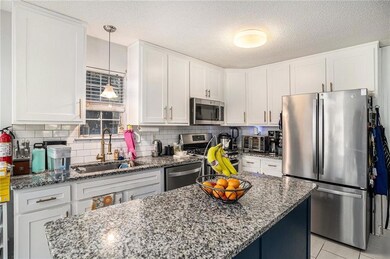 Kitchen with white cabinetry, stainless steel appliances, light stone counters, decorative backsplash, and a textured ceiling