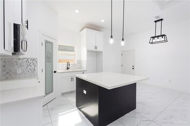 Kitchen featuring light tile floors, white cabinets, hanging light fixtures, and a center island