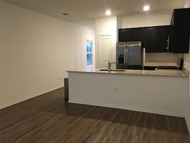 Kitchen with stainless steel fridge, dark cabinets, dark wood-type flooring, and a peninsula
