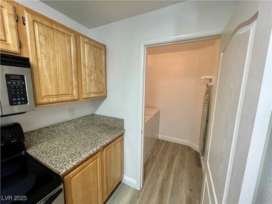 Kitchen featuring black / electric stove, light stone countertops, stainless steel microwave, light wood finished floors, and washing machine and clothes dryer