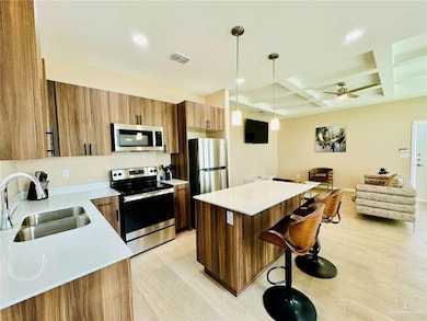 Kitchen with open floor plan, a center island, appliances with stainless steel finishes, decorative light fixtures, and a ceiling fan