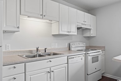 Kitchen featuring white appliances, white cabinetry, light countertops, under cabinet range hood, and dark wood-type flooring