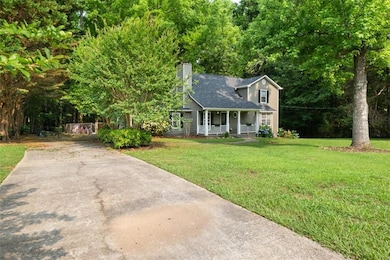 View of front of house with a porch, a front lawn, a chimney, concrete driveway, and a shingled roof