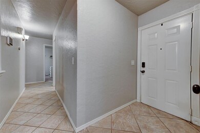 Entrance foyer featuring light tile patterned floors, a textured wall, and baseboards
