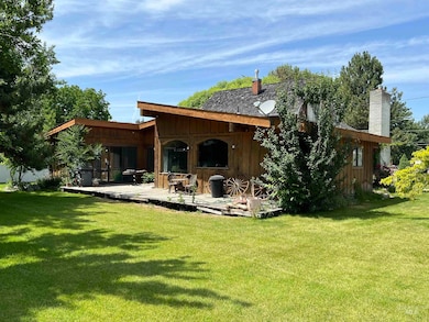 Back of property with a deck, board and batten siding, a chimney, and a lawn