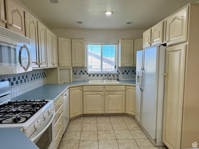 Kitchen featuring white appliances, light countertops, tasteful backsplash, light tile patterned floors, and recessed lighting