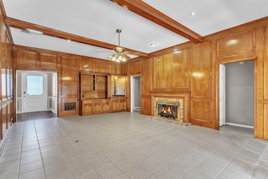 Unfurnished living room with wood walls, beamed ceiling, a brick fireplace, ceiling fan, and light tile patterned floors