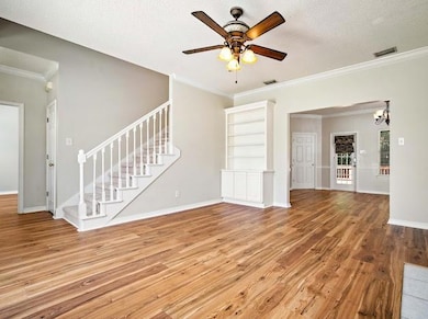 Unfurnished living room with wood finished floors, stairway, a ceiling fan, crown molding, and a chandelier